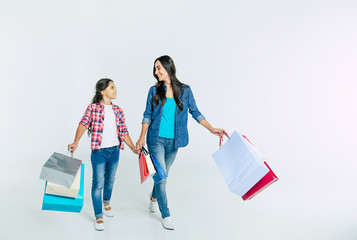 Beautiful mother and cute daughter in casual clothes with shopping bags in hands make purchases at...