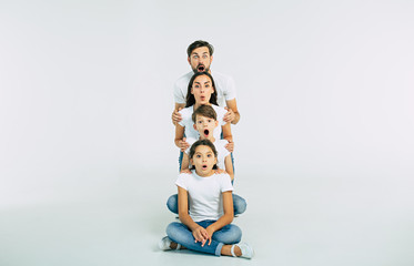It's impossible! Very surprised family with opened mouths looking on camera isolated on white in T-shirts