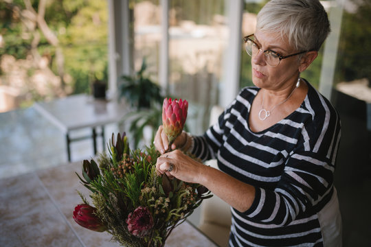 Portrait of a senior woman adding a protea flower to a bouquet. Elderly woman enjoying arranging flowers as a hobby