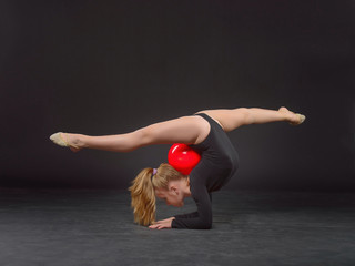Young beautiful white caucasian girl gymnast doing gymnastic exercise with a red sports ball on...