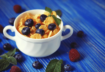 Healthy eating, food and diet concept - Cornflakes with berries raspberries and blueberries on blue wooden background.