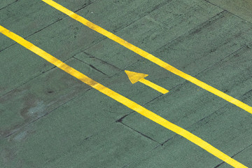 Fototapeta premium Directional traffic yellow arrow on a green tarmac texture floor.