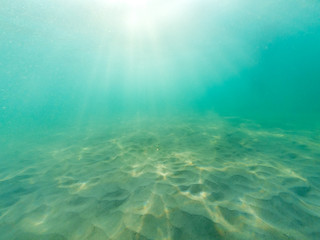 Fototapeta na wymiar Underwater blue sea background. Underwater view of ocean, sand and sun lights.