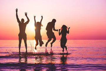 Happy friends jumping inside water on tropical beach at sunset