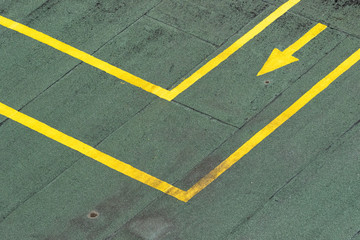 Directional traffic yellow arrow on a green tarmac texture floor.