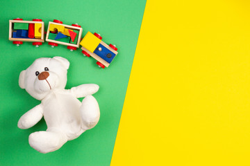 Baby kids toys background. White teddy bear and wooden toy train on multicolored yellow and green background