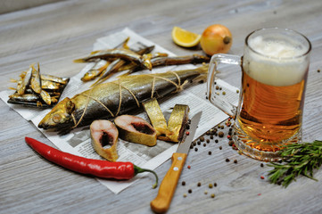 A glass of beer and smoked fish on the newspaper are a traditional beer appetizer. Light wooden background.