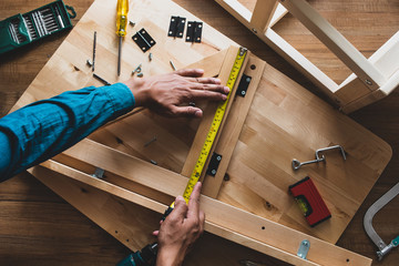 Man assembly wooden furniture,fixing or repairing house with yellow tape measures