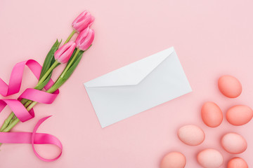 top view of greeting envelope, tulips with ribbon and easter eggs isolated on pink