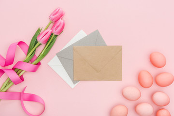top view of greeting envelopes, tulips and easter eggs isolated on pink