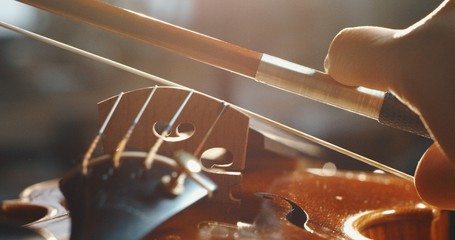 Artistic macro close up of master artisan luthier playing with a bow on a handmade violin or cello.