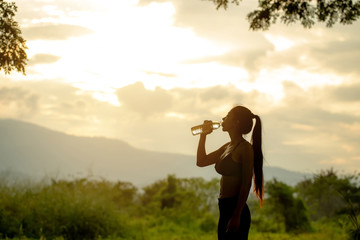 Sport asian girl drinking water from recycled plastic bottle in the mountains in the evening.