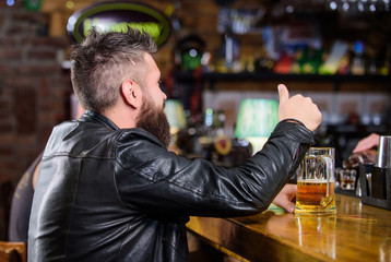 Bar is relaxing place to have drink and relax. Man with beard spend leisure in dark bar. Hipster relaxing at bar with beer. Brutal hipster bearded man sit at bar counter drink beer. Friday evening
