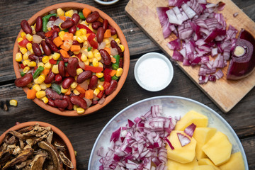 Mixture of vegetables, dried boletus mushrooms, sliced potato, red onion sliced and whole on a cutting board and spices, on old rustic wooden table.
