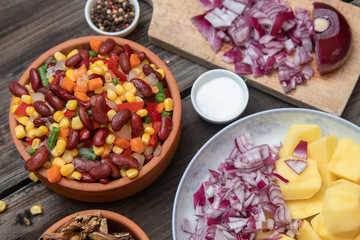 Mixture of vegetables, dried boletus mushrooms, sliced potato, red onion sliced and whole on a cutting board and spices, on old rustic wooden table.