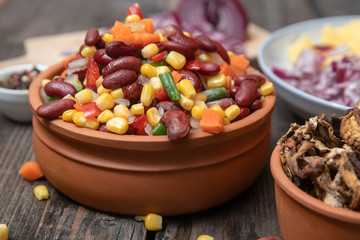 Mixture of vegetables, dried boletus mushrooms, sliced potato, red onion sliced and whole on a cutting board and spices, on old rustic wooden table.