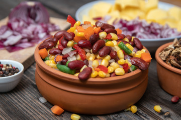 Mixture of vegetables, dried boletus mushrooms, sliced potato, red onion sliced and whole on a cutting board and spices, on old rustic wooden table.