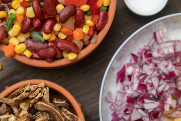 Mixture of vegetables, dried boletus mushrooms, sliced potato, red onion sliced and whole on a cutting board and spices, on old rustic wooden table.