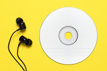 Compact disc and earbuds on yellow background
