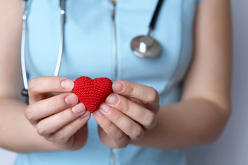Cardiology and health care, woman doctor holding red knitted heart in hands. Concept of...