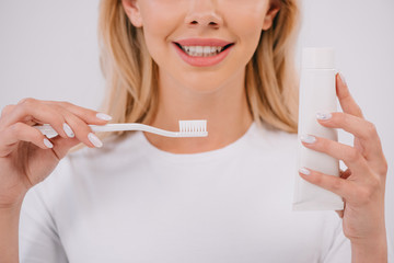 cropped view of smiling woman holding toothbrush and toothpaste with copy space isolated on white