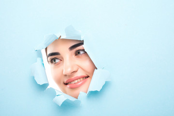 the face of a young beautiful girl with a bright make-up and puffy blue lips peers into a hole in...