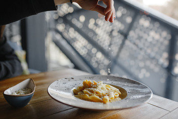 the hand that throws cheese over food, dish from spaghetti and cheese on the plate