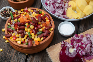 Mixture of vegetables, dried boletus mushrooms, sliced potato, red onion sliced and whole on a cutting board and spices, on old rustic wooden table.