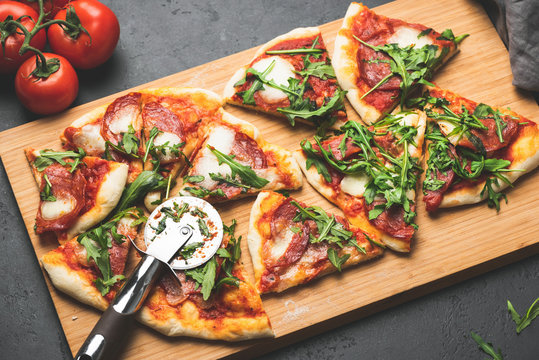 Pizza Or Flatbread With Arugula, Salami, Cheese Sliced On Wooden Cutting Pizza Board