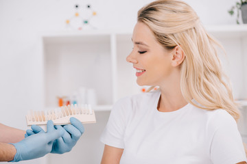 beautiful woman looking at dentist holding teeth color palette in clinic