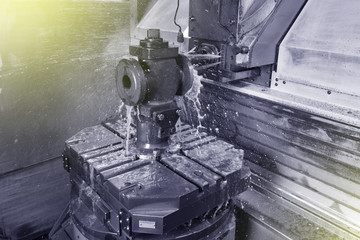 The process of drilling and grinding holes in the body of the valve on the CNC machine. Yellow-green coolant splashes into place