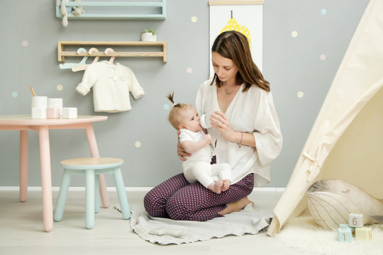Mother or baby sitter speding time with adorable baby girl in the kid's bedroom