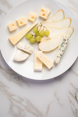 Käseteller mit Edamer, Parmesan, Blauschimmel Käse und Ziegenkäse an Birne und Trauben auf Teller und Marmor Hintergrund
