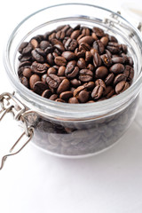 Close up dark roasted coffee beans in a glass jar on white cotton fabric background in natural light