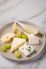 Käseteller mit Edamer, Parmesan, Blauschimmel Käse und Ziegenkäse an Birne und Trauben auf Teller und Marmor Hintergrund