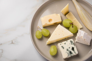 Käseteller mit Edamer, Parmesan, Blauschimmel Käse und Ziegenkäse an Birne und Trauben auf Teller und Marmor Hintergrund