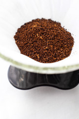 Dark roasted ground coffee in white paper filter on white cotton fabric table top in natural light