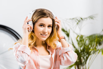 Charming young woman listening music in headphones and looking at camera