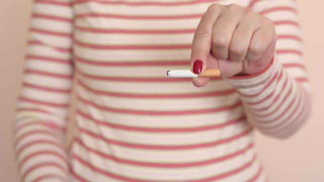 Hands of a woman cutting a cigarette in two halves with scissors. Stop smoking concept.