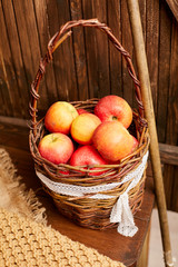 A wicker basket with apples stands on a table in a wooden house