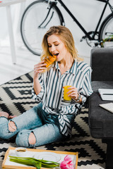 Blonde woman in striped shirt eating croissant and holding glass of orange juice