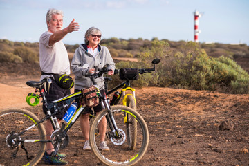 Cheerful caucasian adult senior couple with mountain bike doing healthy sport outdoor leisure activity together - Old people enjoy elderly riding in the nature and enjoying lifestyle