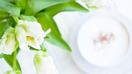 White tulips and cappuccino with cinnamon on a light wooden background. 16:9