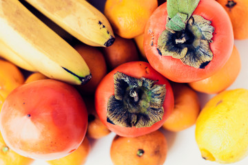A selection of arranged different fresh fruits of bananas, mandarins, persimmons and lemons on white background close upю