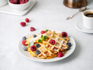 Belgian waffles with raspberries, blueberries, curd and coffee, side view. Healthy homemade breakfast, light concrete background