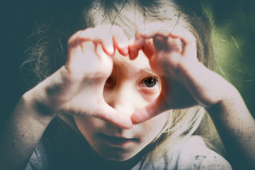 a girl with white hair makes a heart and looks into it. Concept view in childhood. there is toning