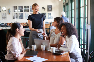 Businesswomen Paying Bill At Meeting Around Table In Coffee Shop
