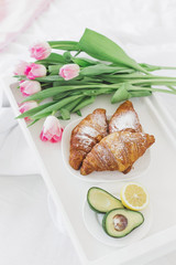Food and tulips in bed. Avocado, croissant and flowers in the morning