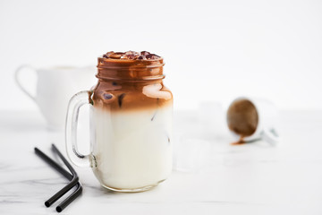 Ice coffee with milk in mason jar and black metal drinking straws on white marble table over white background. Copy space for text.