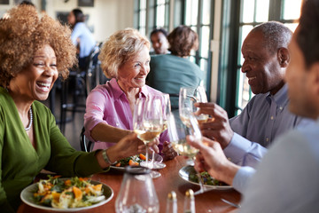 Group Of Smiling Senior Friends Meeting For Meal In Restaurant - Powered by Adobe